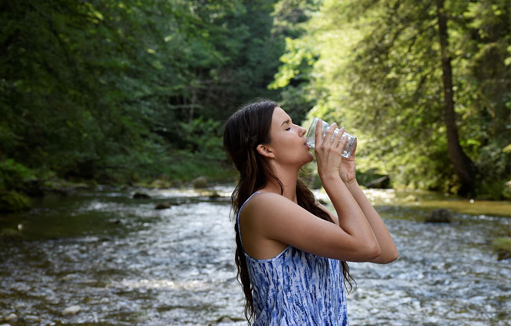 mujer bebiendo una botella de agua en un río en verano