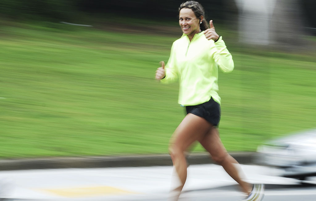 mujer deportista corriendo por la calle y con el dedo pulgar de la mano levantado