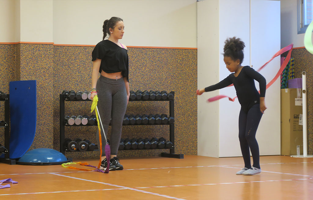 una profesora enseña a una alumna a mover una cinta de gimnasia rítmica