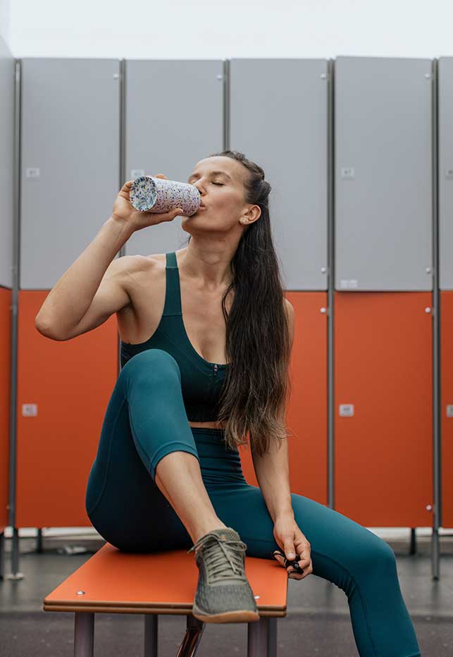 una mujer bebe agua en un vestuario de un gimnasio