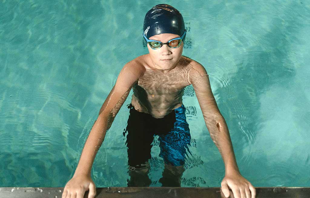 niño con atuendo de natación agarrado al bordillo de la piscina