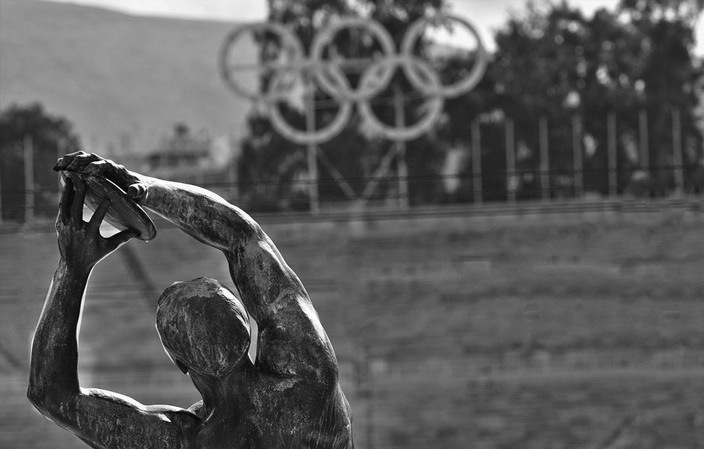 Estatua de un hombre lanzando un disco frente a los aros olímpicos