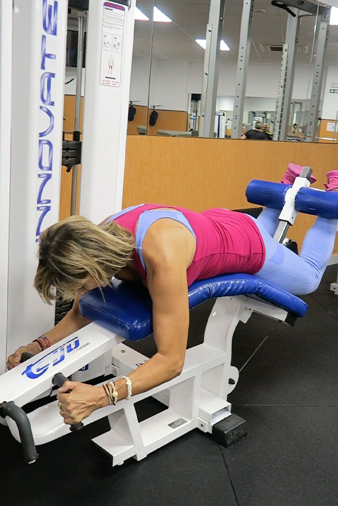 mujer utiliza una máquina de flexión de isquiotibiales en el gimnasio